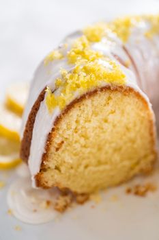 Sliced lemon bundt cake decorated with lemon zest on a cake stand.