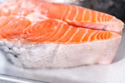 Farm-raised salmon steaks on a cooking tray with a parchment paper.