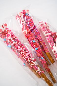 Chocolate-covered pretzel rods decorated with heart-shaped sprinkles for Valentine's Day packaged in a clear bags.