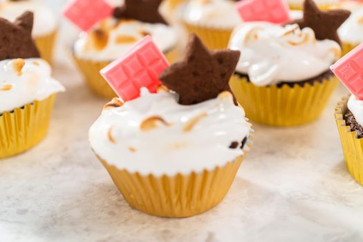 Gourmet s'mores cupcakes with meringue frosting and garnished with star-shaped chocolate graham cracker and a mini pink chocolate bar.