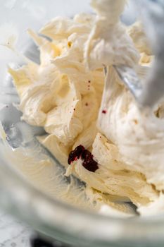 Mixing ingredients in kitchen electric mixer to make ombre pink buttercream frosting.