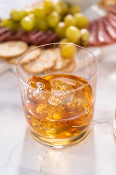 Scotch on the rocks in whiskey glass on a white marble surface.