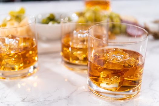 Scotch on the rocks in whiskey glass on a white marble surface.