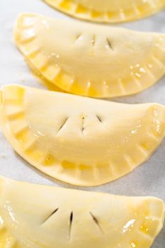 Brushing uncooked empanadas with blueberries with egg wash.