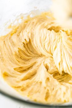 Mixing ingredients with a hand mixer in a large mixing bowl to bake mini vanilla cupcakes with ombre pink buttercream frosting.