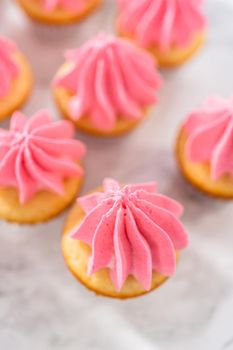 Piping ombre pink buttercream frosting on mini vanilla cupcakes.