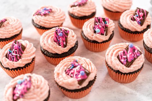 Freshly baked chocolate strawberry cupcakes garnished with gourmet mini pink chocolates.