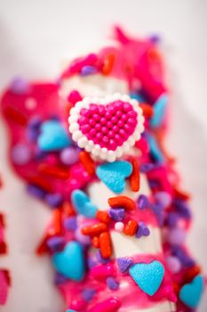 Chocolate-covered pretzel rods decorated with heart-shaped sprinkles for Valentine's Day.