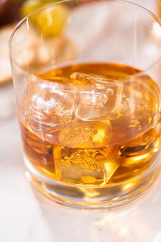 Scotch on the rocks in whiskey glass on a white marble surface.