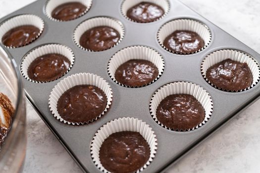 Scooping cupcake batter into the cupcake liners to bake chocolate strawberry cupcakes.