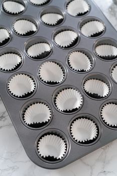 Scooping cupcake batter with dough scoop into a baking cupcake pan with liners to bake mini vanilla cupcakes with ombre pink buttercream frosting.