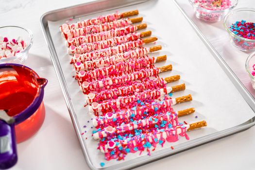 Drizzling melted chocolate over chocolate-dipped pretzels rods and decorating with sprinkles to make chocolate-covered pretzel rods for Valentine's Day.