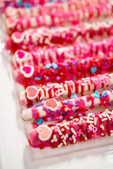 Chocolate-covered pretzel rods decorated with heart-shaped sprinkles for Valentine's Day.