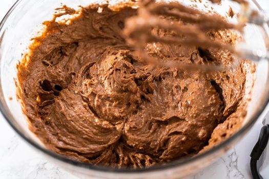 Mixing wet ingredients in a large glass mixing bowl to bake red velvet cupcakes with white chocolate ganache frosting.