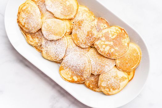 Flat lay. Freshly made small pancakes on a kefir base garnished with powdered sugar.