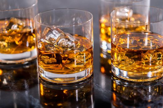 Scotch on the rocks in whiskey glass on a black marble surface.