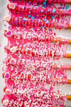 Drizzling melted chocolate over chocolate-dipped pretzels rods and decorating with sprinkles to make chocolate-covered pretzel rods for Valentine's Day.