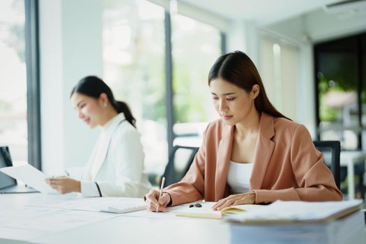 Portrait of a woman using notebooks and budget documents to work on analyzing marketing plans and making plans to increase company profits.