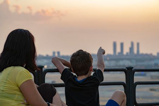 Mom and child looking at Madrid city skyline view during sunset.Kid pointing out the 4 towers silhouette . Kio towers. short from paracuellos de jarama.. 2022