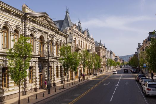 Urban landscape. Large avenue with a wide roadway. Tall historic houses, green trees. Old city. Tbilisi. Architecture of the 60s, neoclassical. Summer, sunny day.