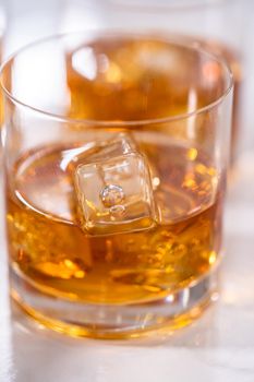 Scotch on the rocks in whiskey glass on a white marble surface.