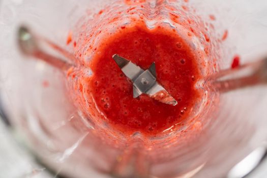 Blending fresh strawberries in a kitchen blender to prepare the strawberry buttercream frosting.