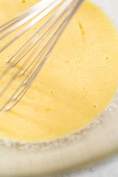 Mixing ingredients in a glass mixing bowl with a blending whisk to bake chocolate strawberry cupcakes.