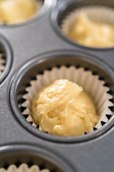 Scooping cupcake batter with dough scoop into a baking cupcake pan with liners to bake mini vanilla cupcakes with ombre pink buttercream frosting.