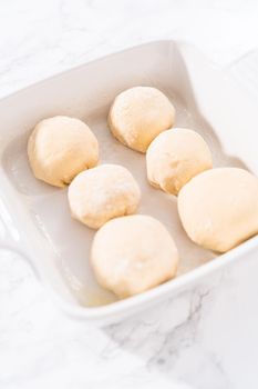 Rising dough in a white ceramic dish to prepare dinner rolls.