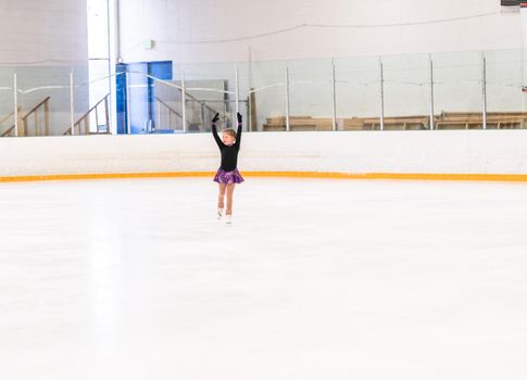 Little girl practicing figure skating on indoor ice skating rink.