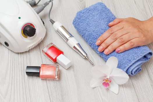 Milling cutter, nail polishes and a female hand on a towel on gray wooden background. A set of cosmetic tools for professional hardware manicure. Top view