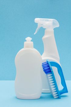 Bottles of dishwashing liquid, glass and tile cleaner, brush on blue background. Washing and cleaning concept.