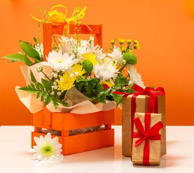 Beautiful bouquet of yellow and white flowers in the wooden basket with gift boxes.