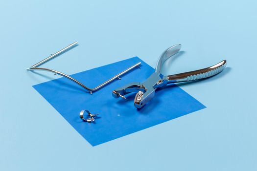 Dental hole punch, the clamp, the metal frame and the rubber dam on the blue background. Medical tools concept.