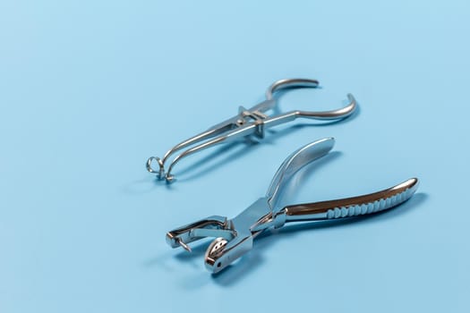 Rubber dam forcep and the dental hole punch on the blue background. Medical tools concept. Top view.