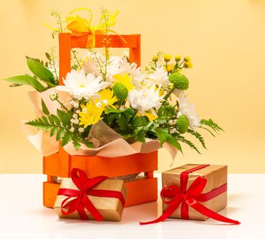 Beautiful bouquet of yellow and white flowers in the wooden basket with gift boxes.