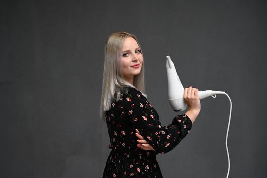 Beautiful smiling girl with blonde long straight hair using hairdryer. Portrait of happy female using blow hair dryer. Hairstyle, hair care concept. High resolution