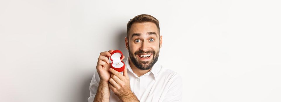 Close-up of handsome guy making proposal, looking hopeful and showing wedding ring, asking marry him, white background.