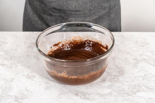 Mixing ingredients in a glass mixing bowl with a blending whisk to bake chocolate strawberry cupcakes.