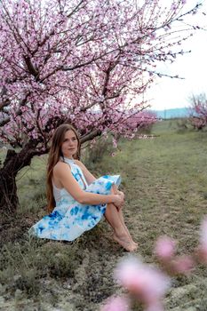 Young beautiful woman in blue dress and long hair is enjoying with blossoming peach trees.