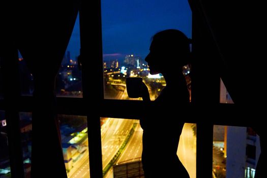 The silhouette of a girl against a stained-glass window looks at the night city.