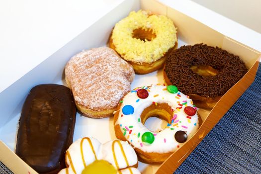 Box of sweets filled with colorful donuts and eclairs.