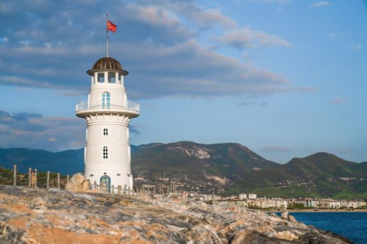 Turkey, Alanya - November 9, 2020: White port lighthouse on the background of mountains and sky and sea. Copy space