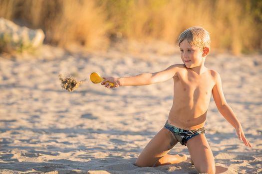 Little blond boy playing with small colorful plastic sand toy on the beach, kid building a sandcastle with fun, active happy summer holiday.