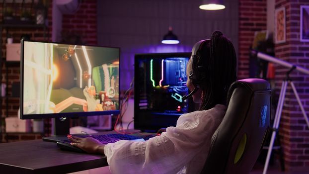 African american gamer girl using pc gaming setup having a good time playing multiplayer online action game in home living room. Woman streaming first person shooter while talking in headset.