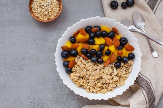 Oatmeal porridge with blueberries, mango and almonds in bowl on concrete grey table from above. flatlay. Healthy breakfast food. Copy space