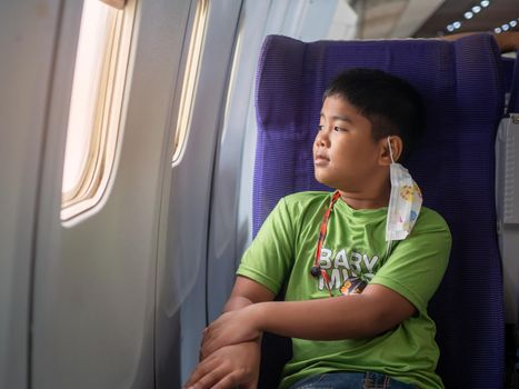 An Asian boy sits and smiles and looks out the window of an airplane.