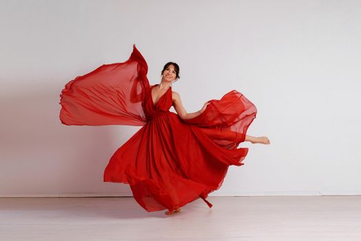 Dancer in a red flying dress. Woman ballerina dancing on a white studio background.