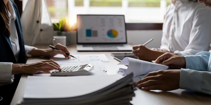 Business bookkeeper working with a calculator to calculate business data summary report, accountancy document and laptop computer at the office, business meeting concept