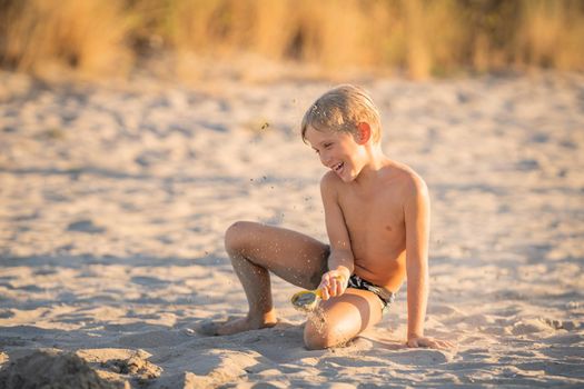 Little blond boy playing with small colorful plastic sand toy on the beach, kid building a sandcastle with fun, active happy summer holiday.